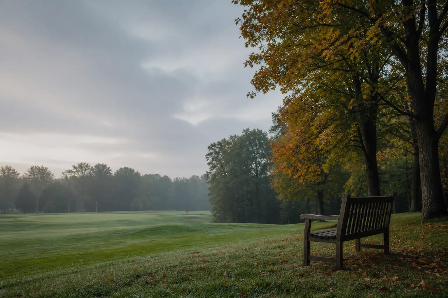 An autumn golf course with a quiet bench beside the fairway.